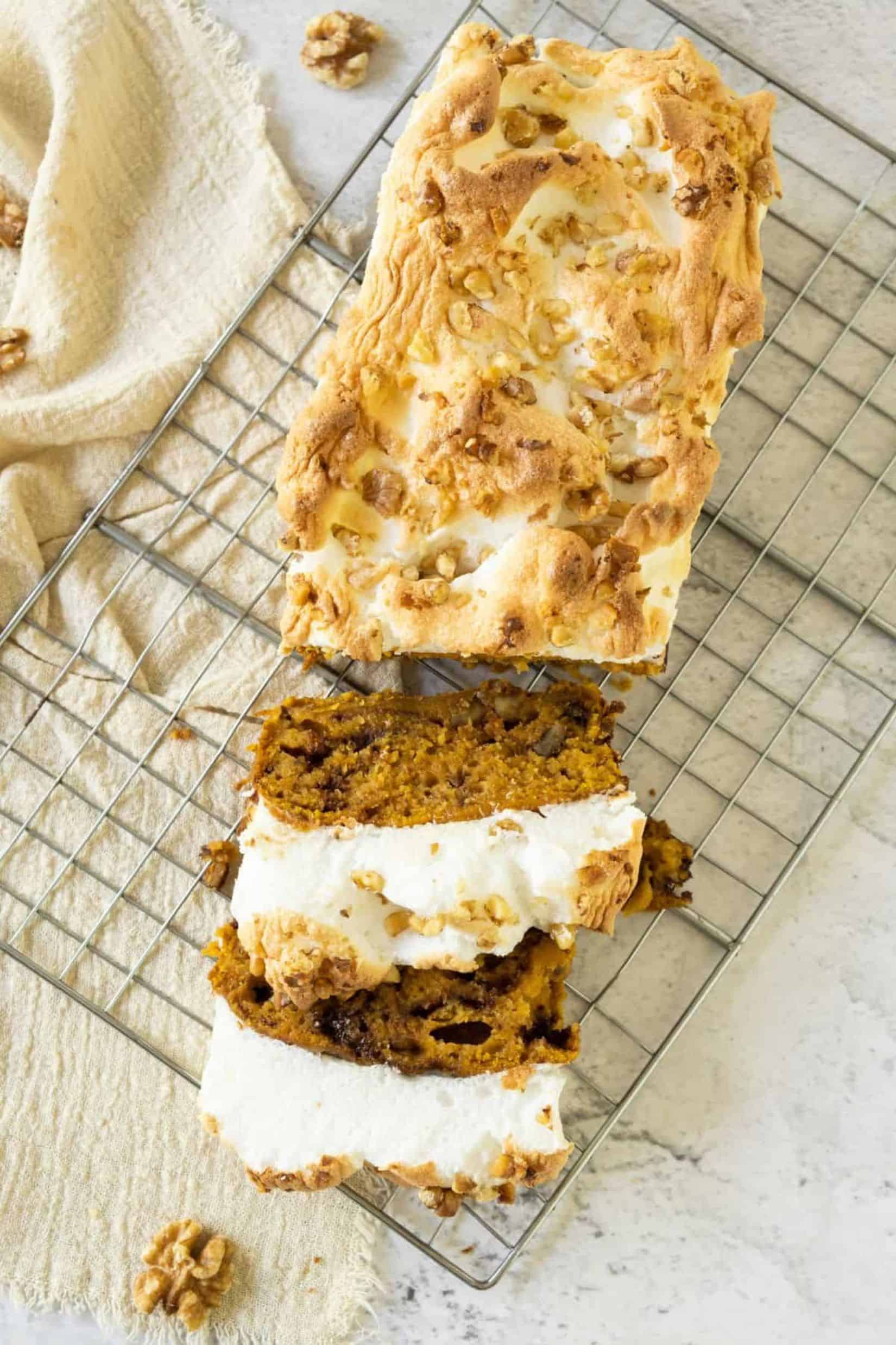 A slice being cut from sweet potato quick bread topped with fluffy meringue, resting on a wire cooling rack.