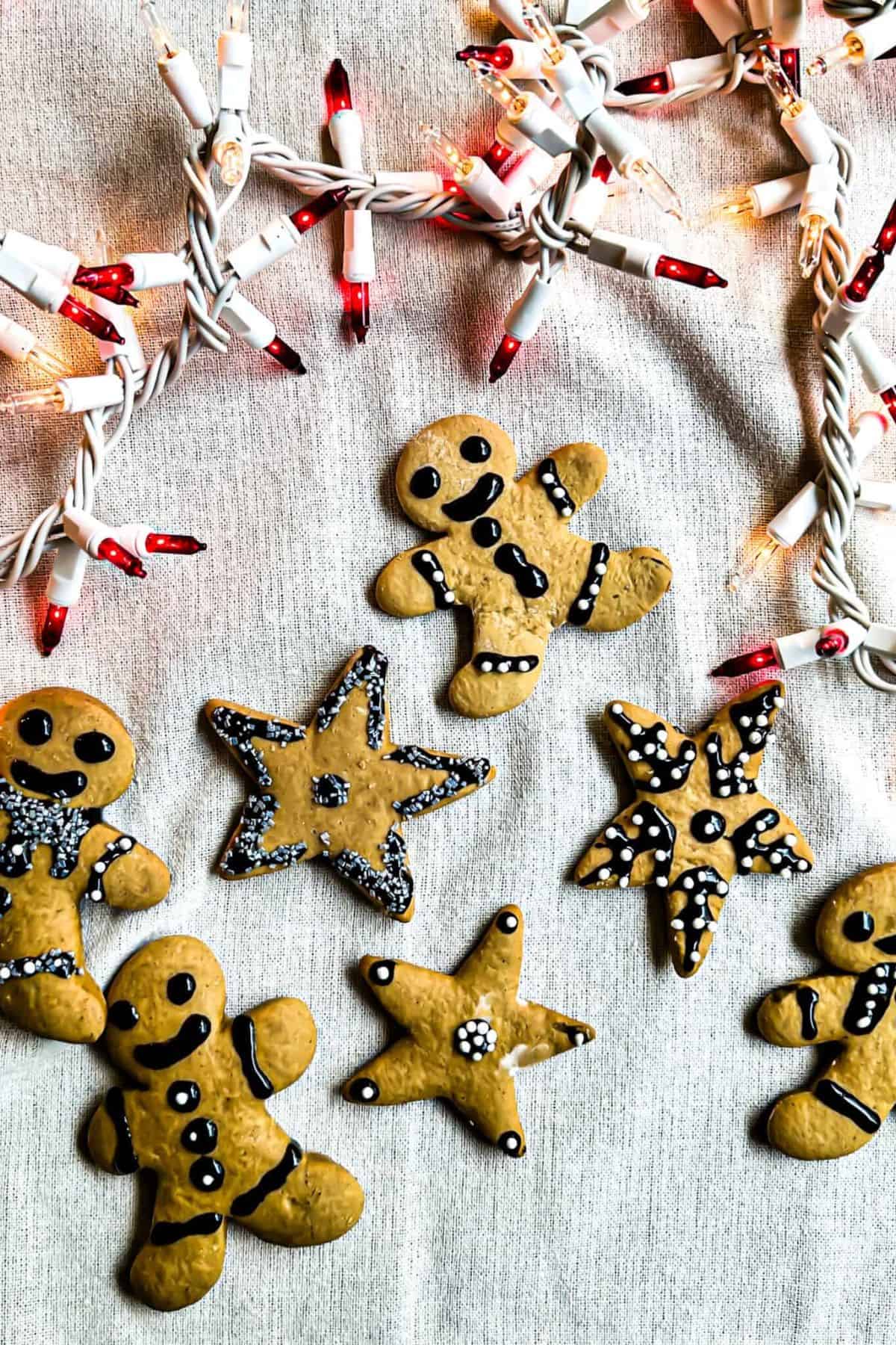 Gingerbread man-shaped cookies decorated with Christmas light designs, placed on a surface with a white cloth underneath.