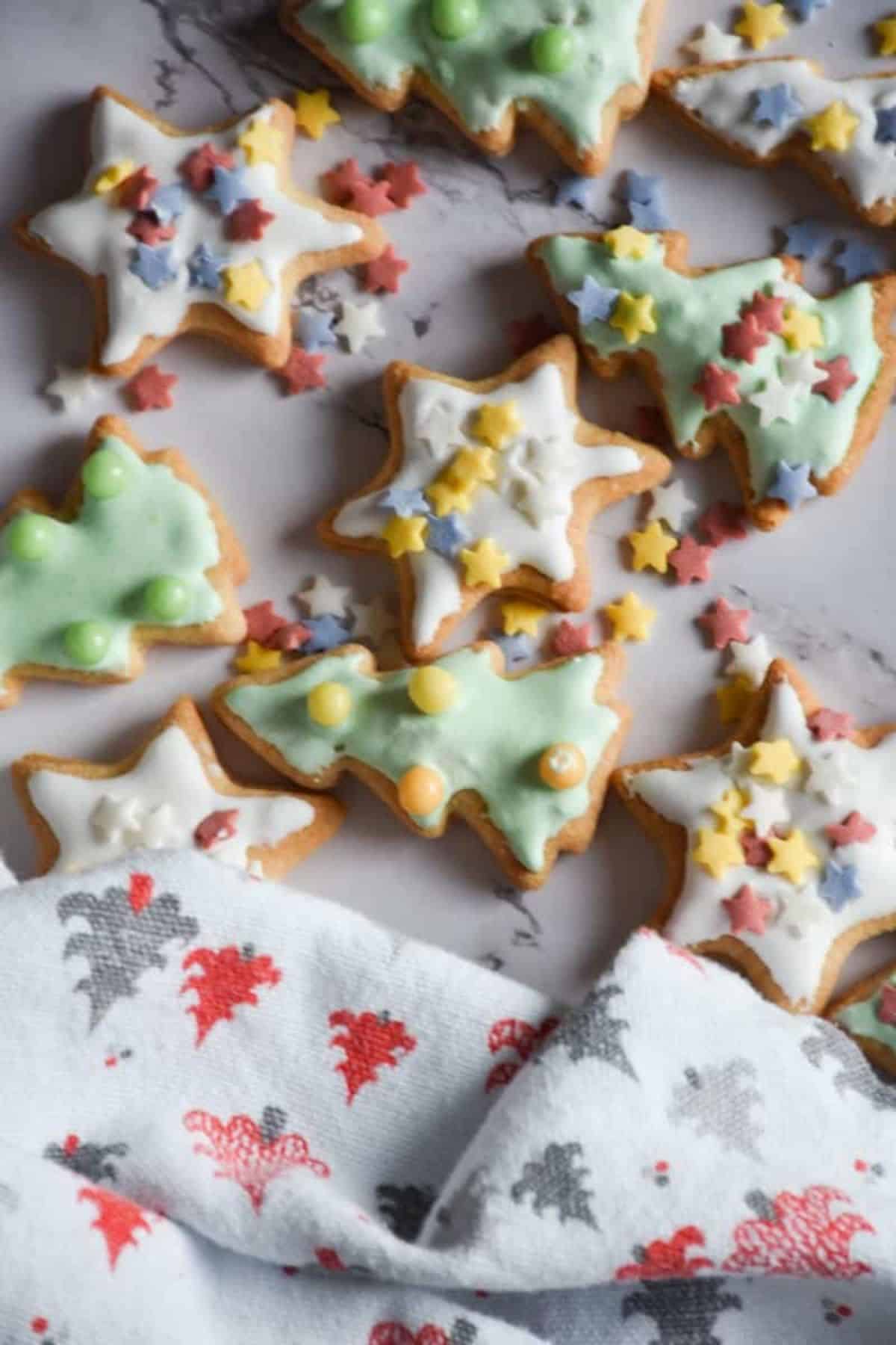 Cut-out Christmas tree-shaped cookies in different colors with sprinkles, scattered on a flat surface.