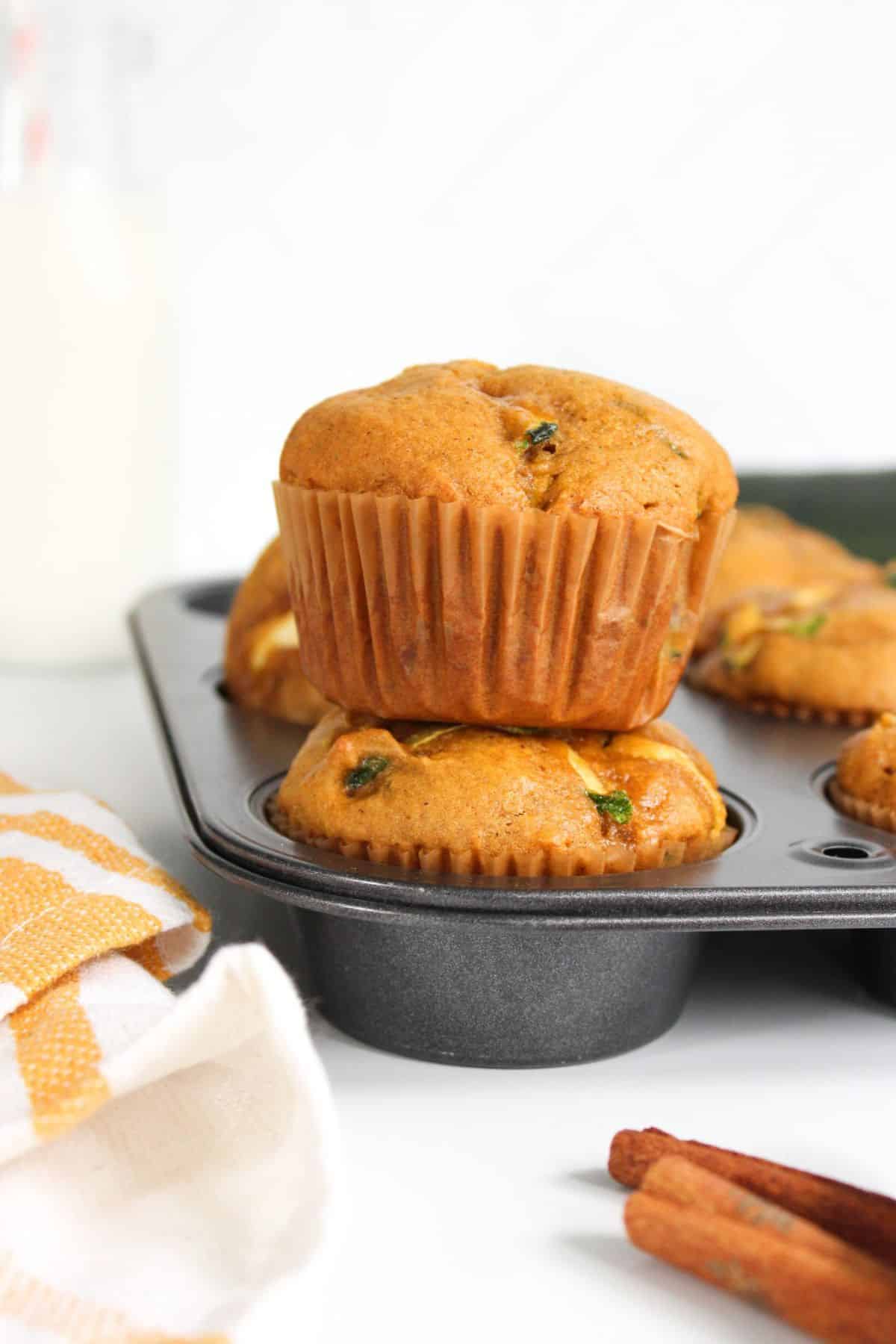 Stacked pumpkin zucchini muffins arranged in a baking tray.