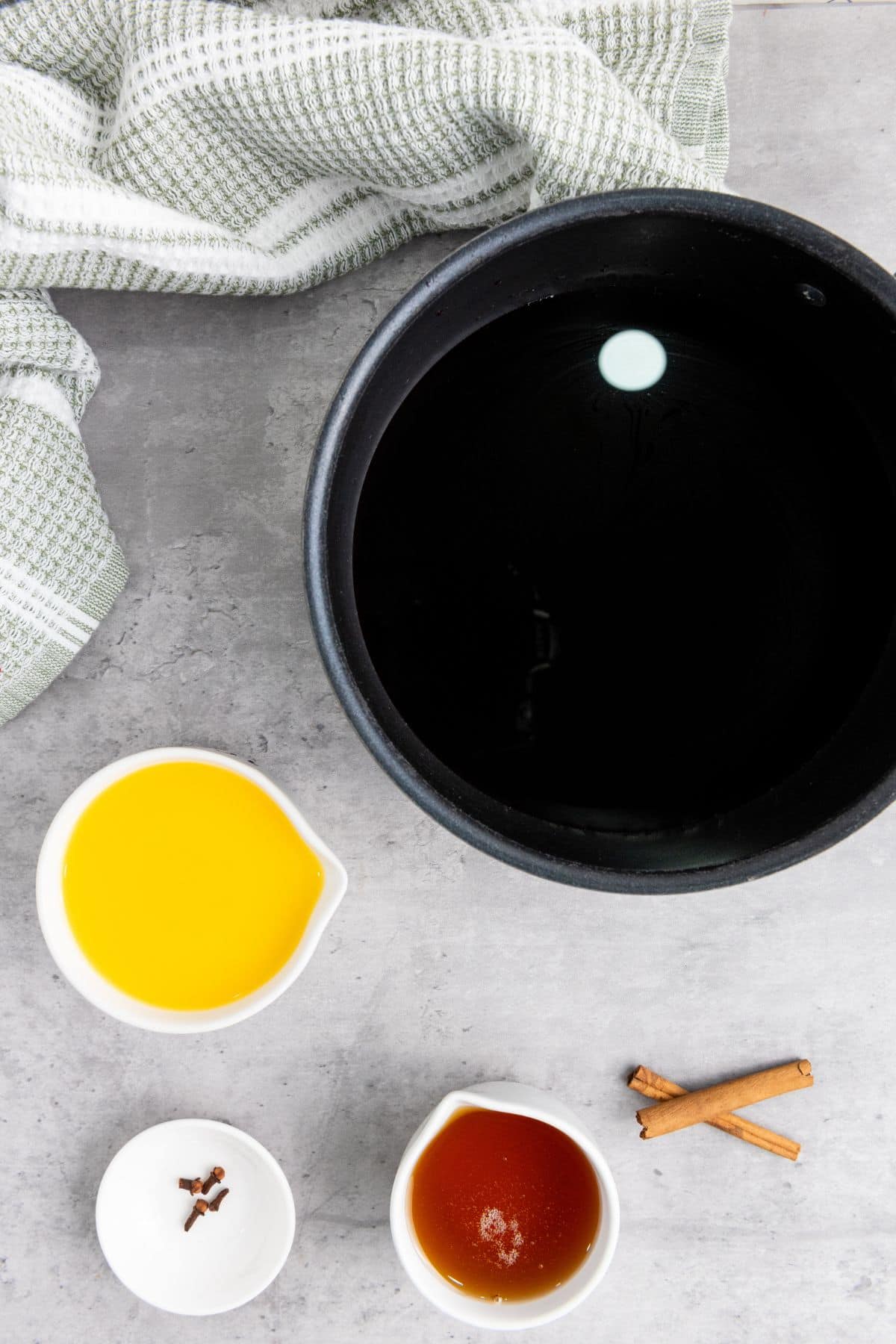 A pot filled with red wine mixture surrounded with other ingredients, ready for poaching pears.