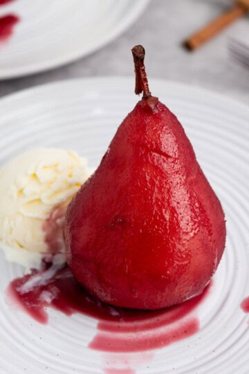 A single pear on a plate, served with a scoop of vanilla ice cream.