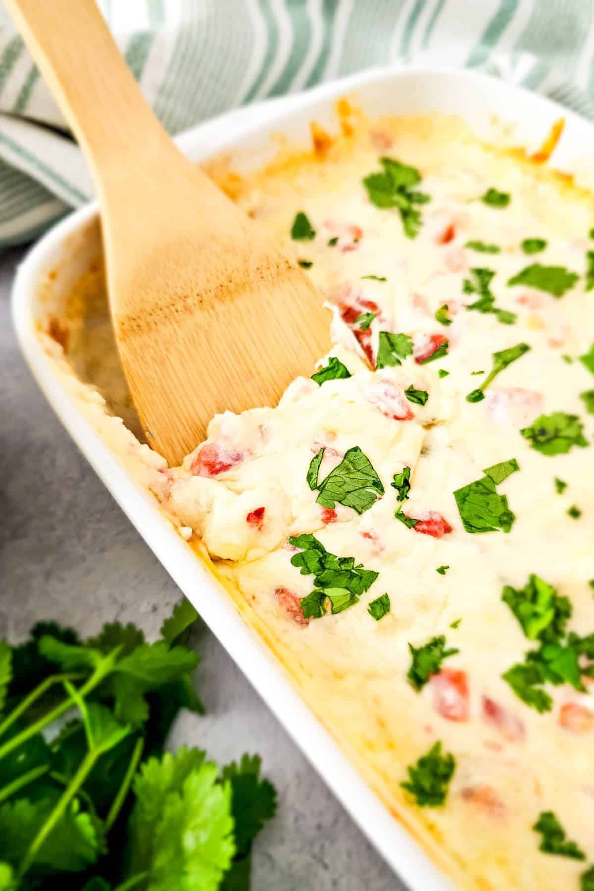 A serving dish filled with loaded queso dip topped with melted cheese and diced tomatoes, with a spatula resting on the side ready for serving.