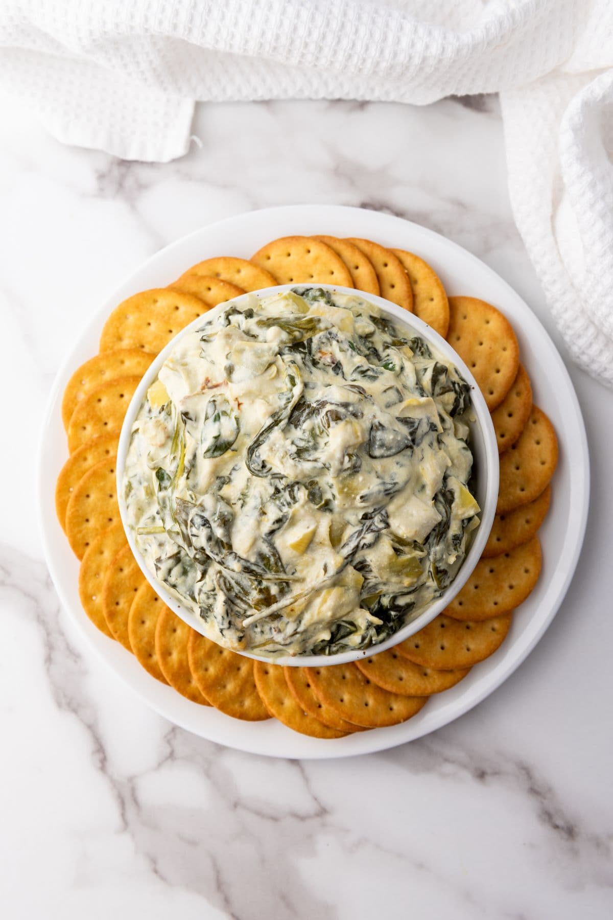 Spinach artichoke dip served in a bowl at the center of a plate, surrounded by biscuits for dipping.