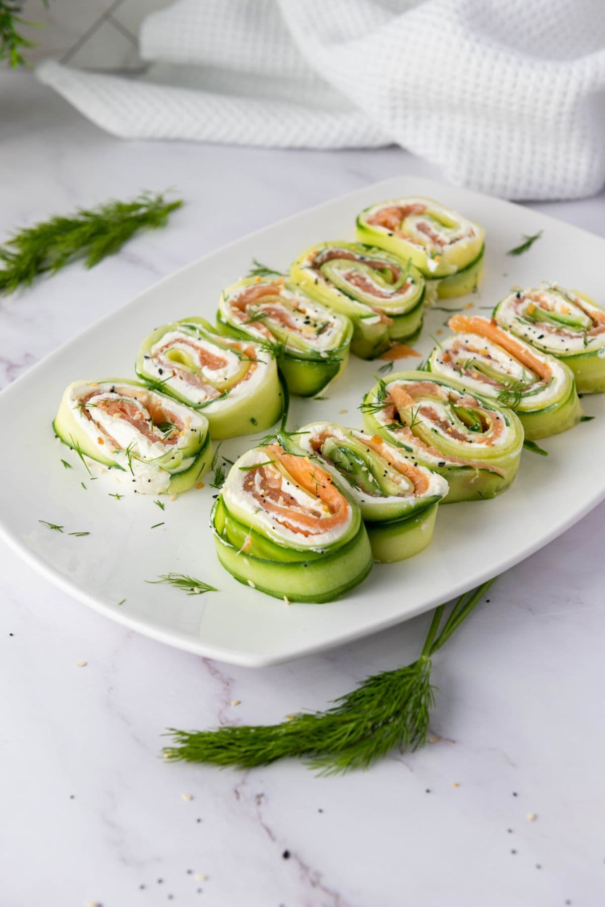 Neatly arranged everything bagel cucumber rolls with smoked salmon on a plate.