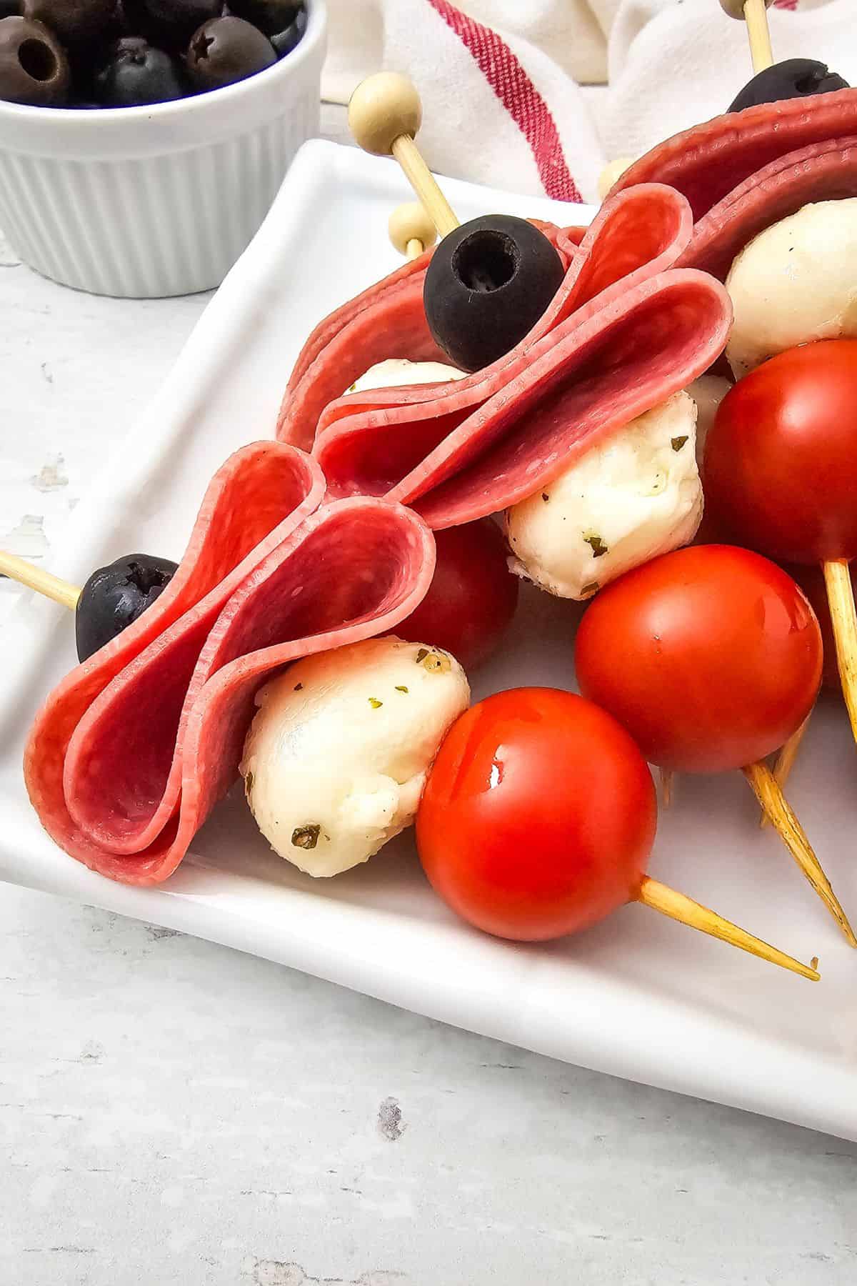 Close-up of colorful antipasto skewers with salami, cherry tomatoes, olives, and marinated mozzarella.
