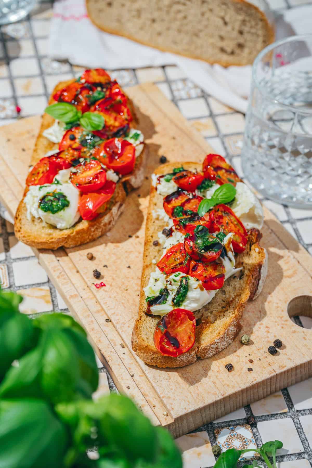 Savory burrata toast with roasted tomatoes and basil drizzle served on a wooden board, garnished with fresh basil leaves.