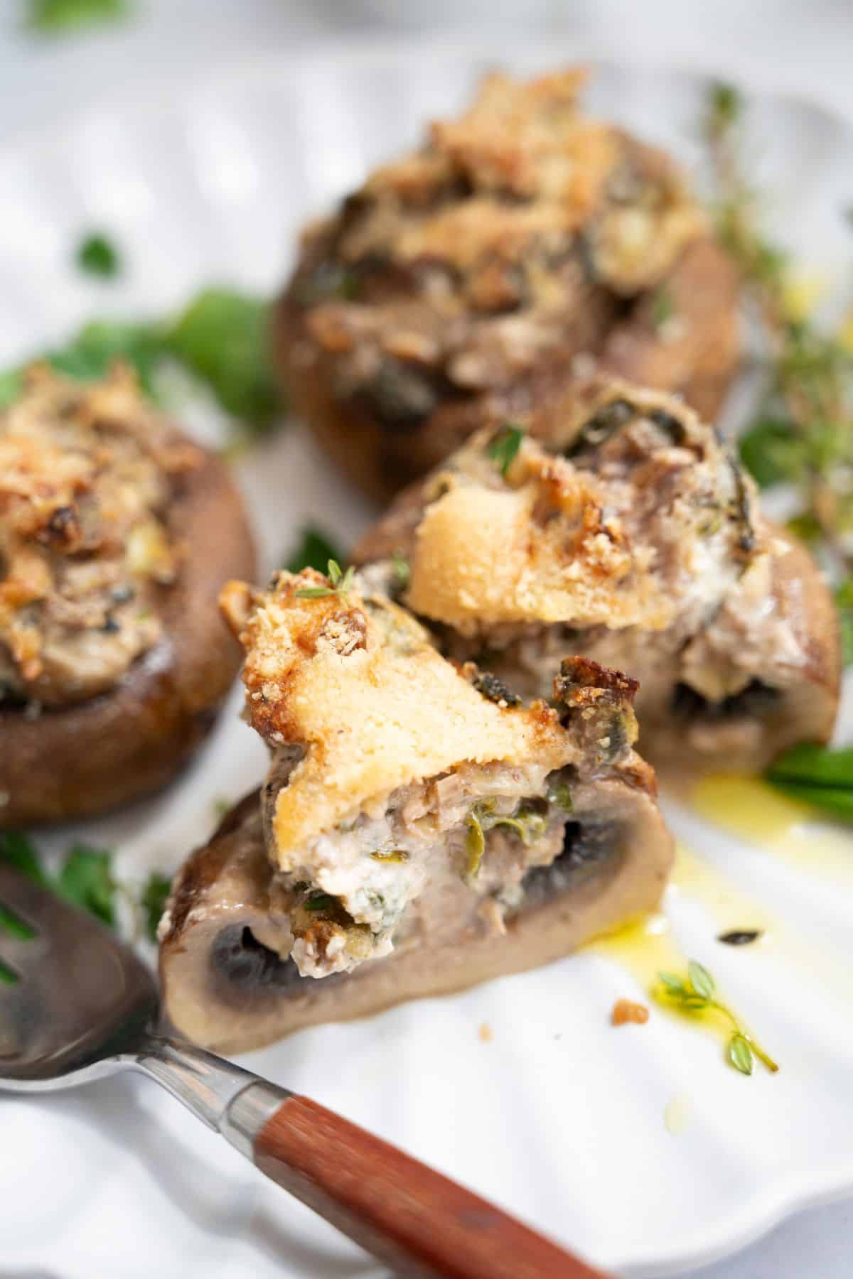 Stuffed mushrooms with spinach and artichokes on a plate, one cut open to show the creamy interior.