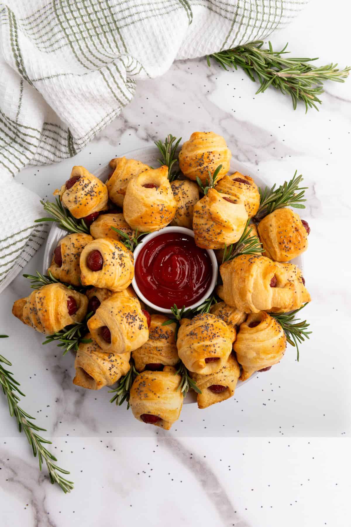 Mini Piggies in a Blanket arranged around a small bowl of dip in the center, with fresh figs placed around the edges.