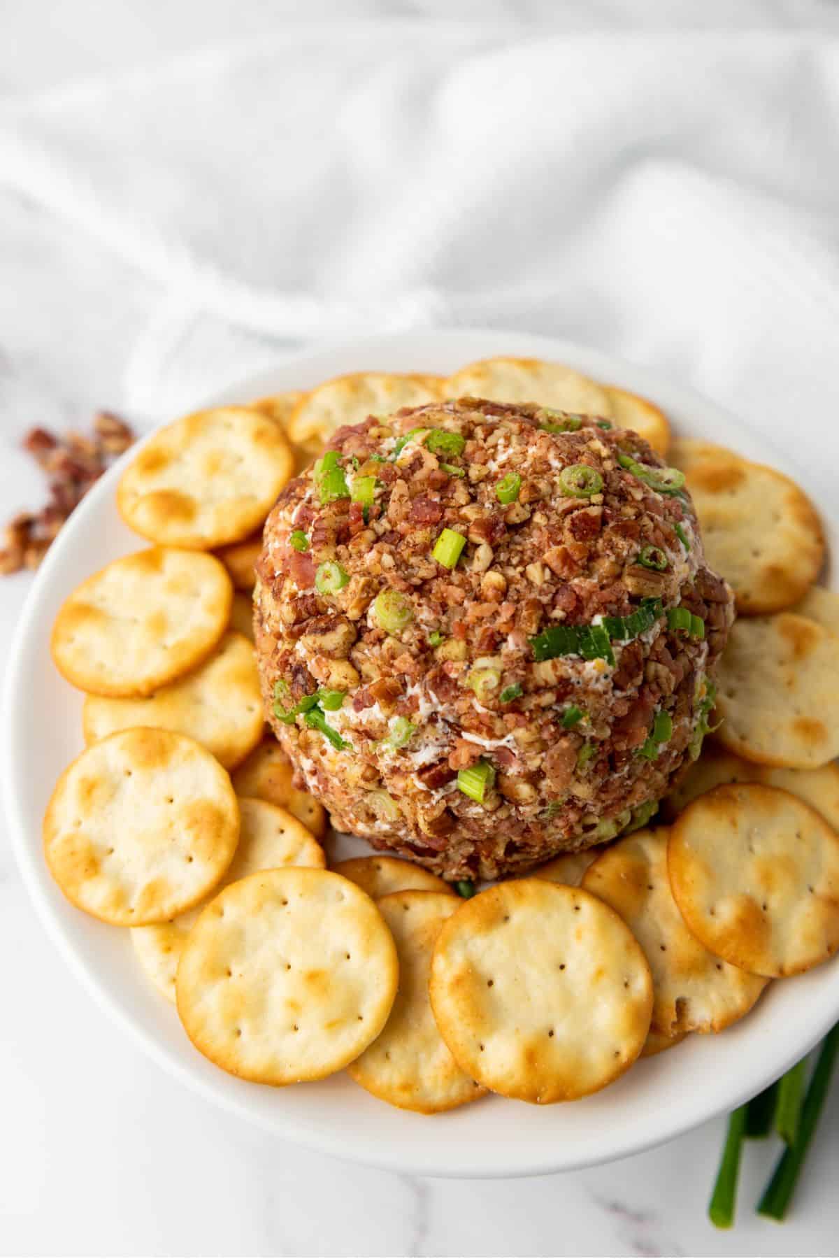 Pecan bacon cheeseball placed in the center of a plate, surrounded by biscuit crackers.