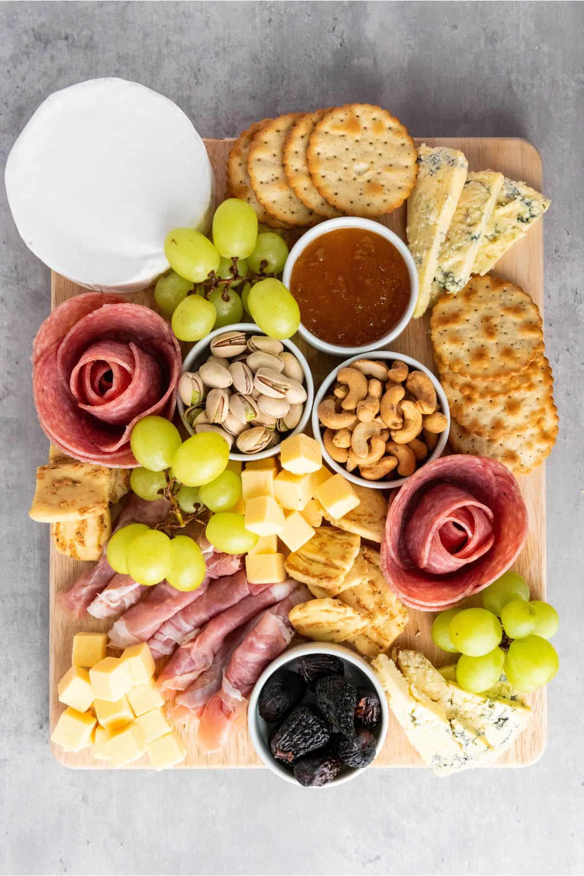 A classic charcuterie board arranged on a wooden board with a mix of cheeses, cured meats, fresh fruits, nuts, and crackers.