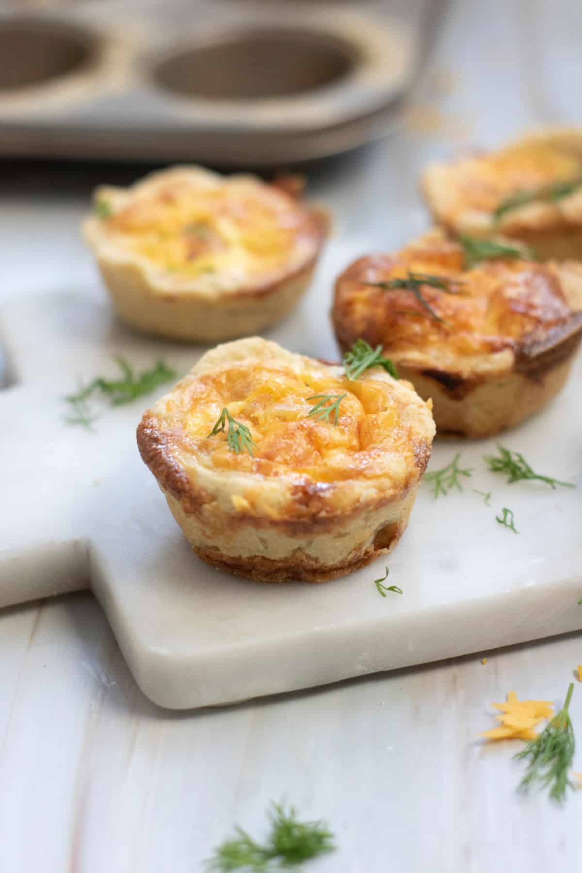 Party-ready salmon quiche bites arranged on a marble board, garnished with fresh herbs.