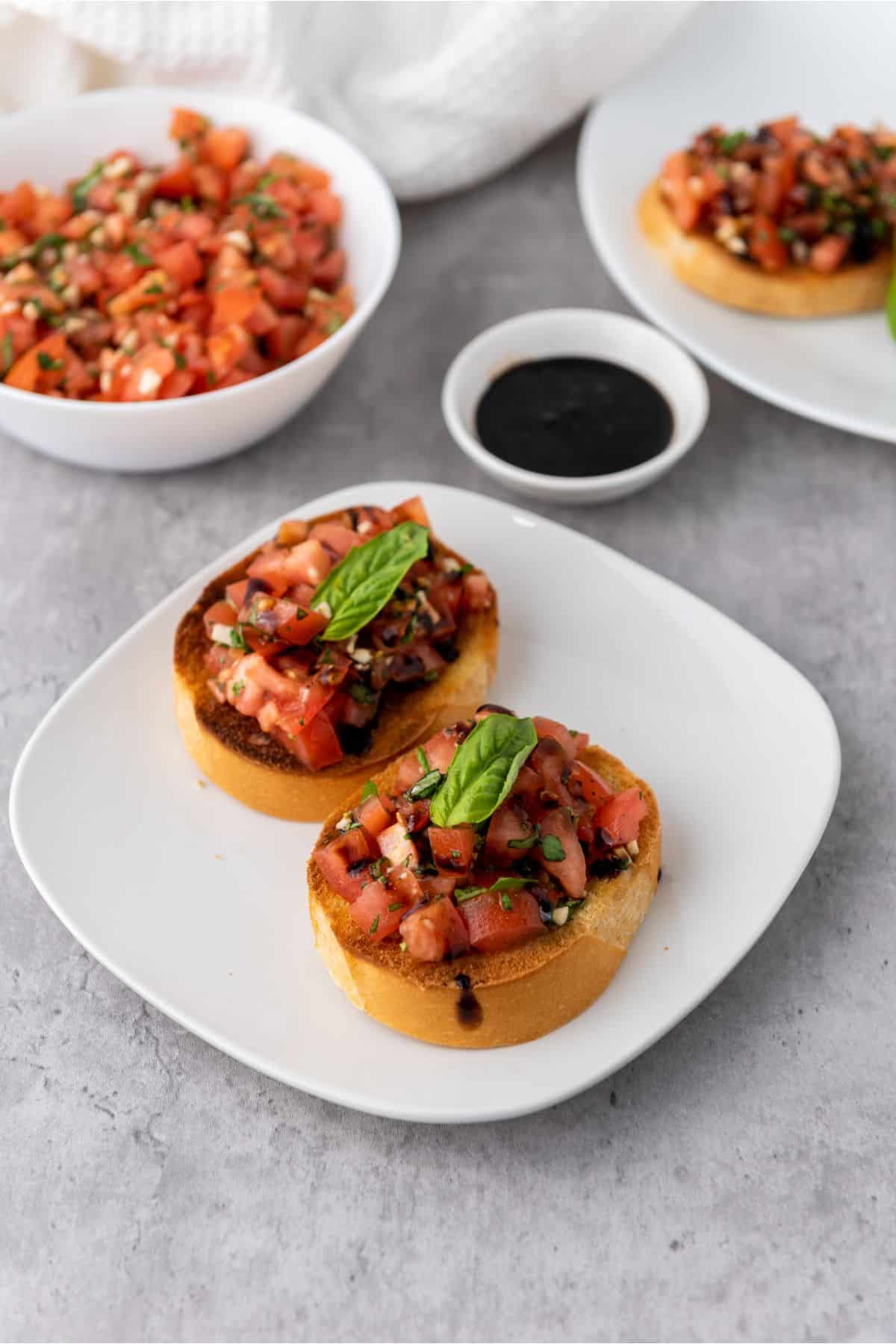 Two pieces of classic Mediterranean bruschetta in a bowl, served with balsamic glaze on the side.