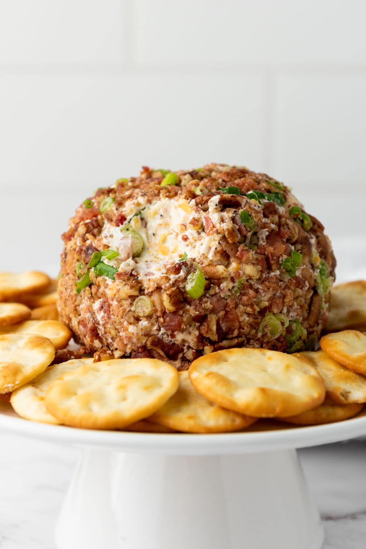 Pecan bacon cheeseball placed in the center of a plate, surrounded by biscuit crackers.