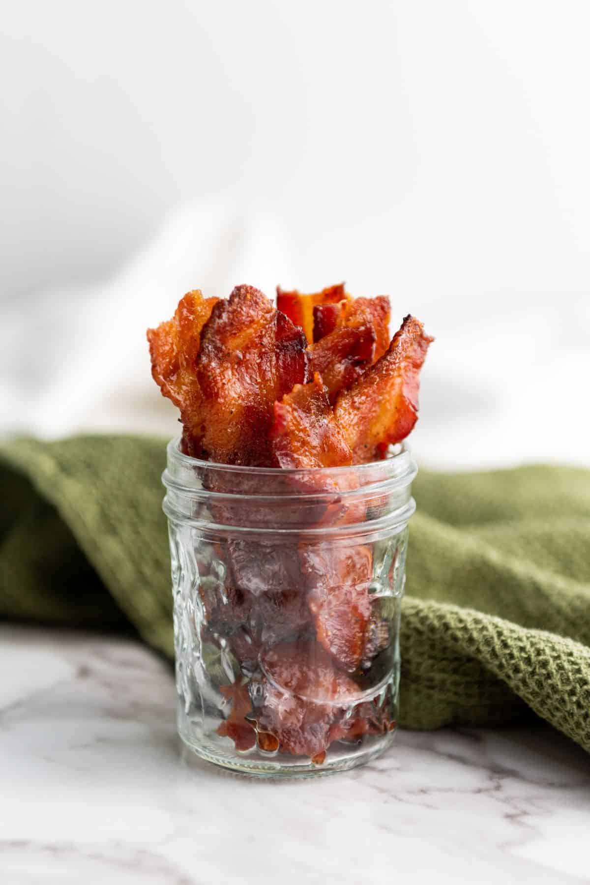 A jar filled with candied maple brown sugar bacon, placed next to a table napkin.