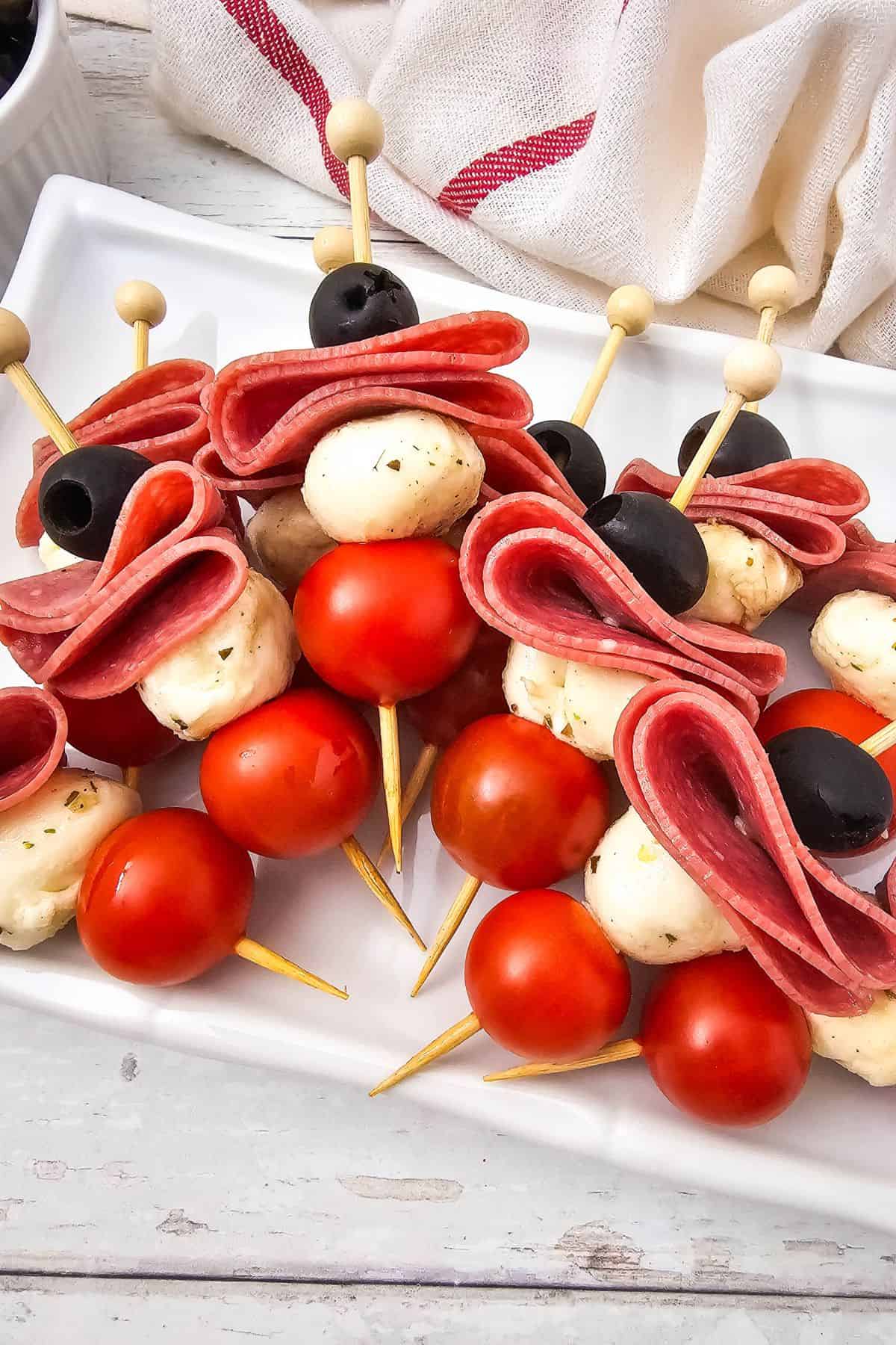 Close-up of antipasto skewers with salami, olives, marinated mozzarella, and cherry tomatoes stacked on skewers.