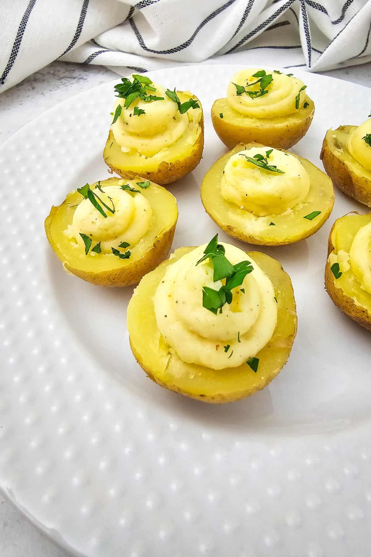 Deviled potatoes arranged on a plate, filled with a creamy seasoned mixture and topped with herbs.