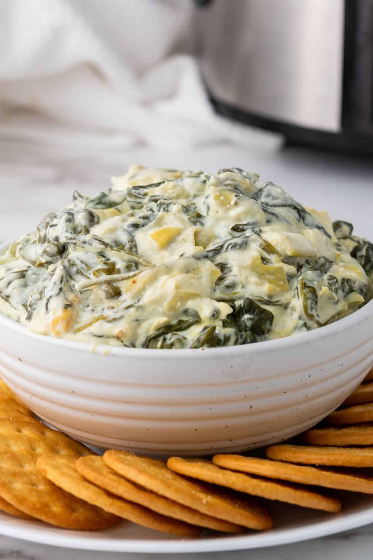 Slow cooker spinach and artichoke dip served in a bowl, surrounded by biscuit crackers.