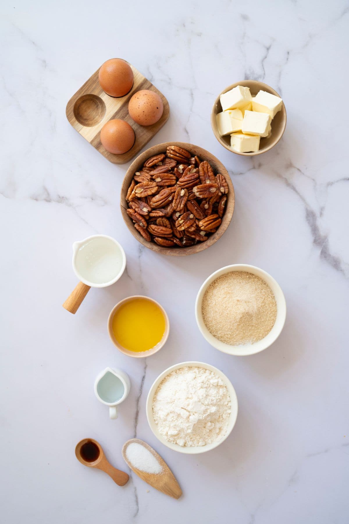 Top-down view of pecan pie ingredients neatly arranged on a marble surface, including flour, butter, eggs, brown sugar, corn syrup, pecans, and a small bowl of salt and vanilla extract.