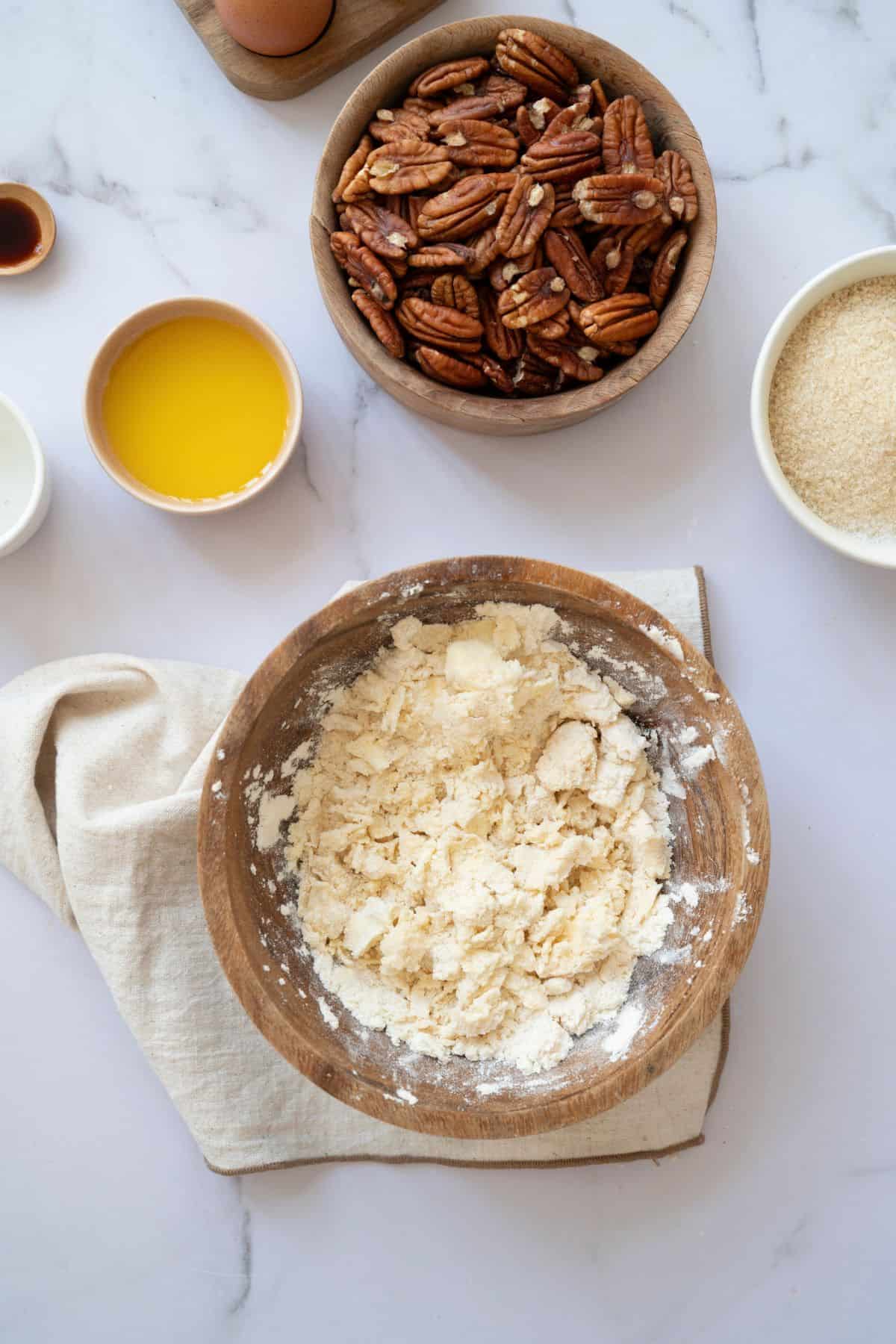 Dry ingredients in a large wooden bowl with a table napkin underneath, surrounded by other pie ingredients on the countertop.