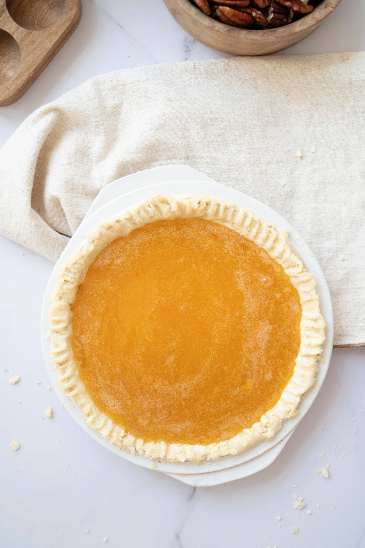 A smooth pie filling being poured into a pie crust, with a table napkin placed underneath the dish.