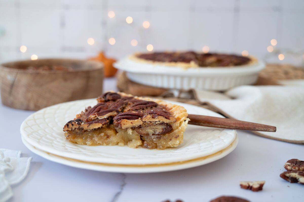 A slice of pie served on a plate with a fork beside it, while the rest of the pie is blurred in the background.