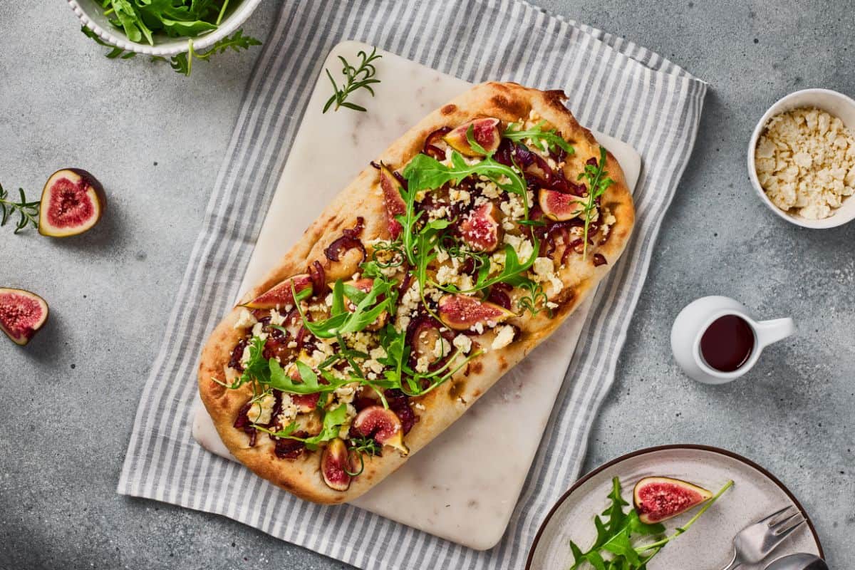Served flatbread garnished with arugula and goat cheese, with a tablecloth underneath.