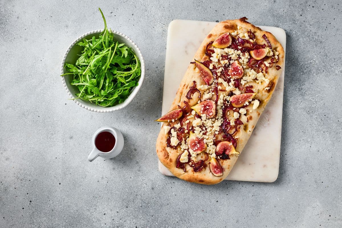 Freshly baked flatbread with figs, caramelized onions, and goat cheese, served with arugula and balsamic on the side.