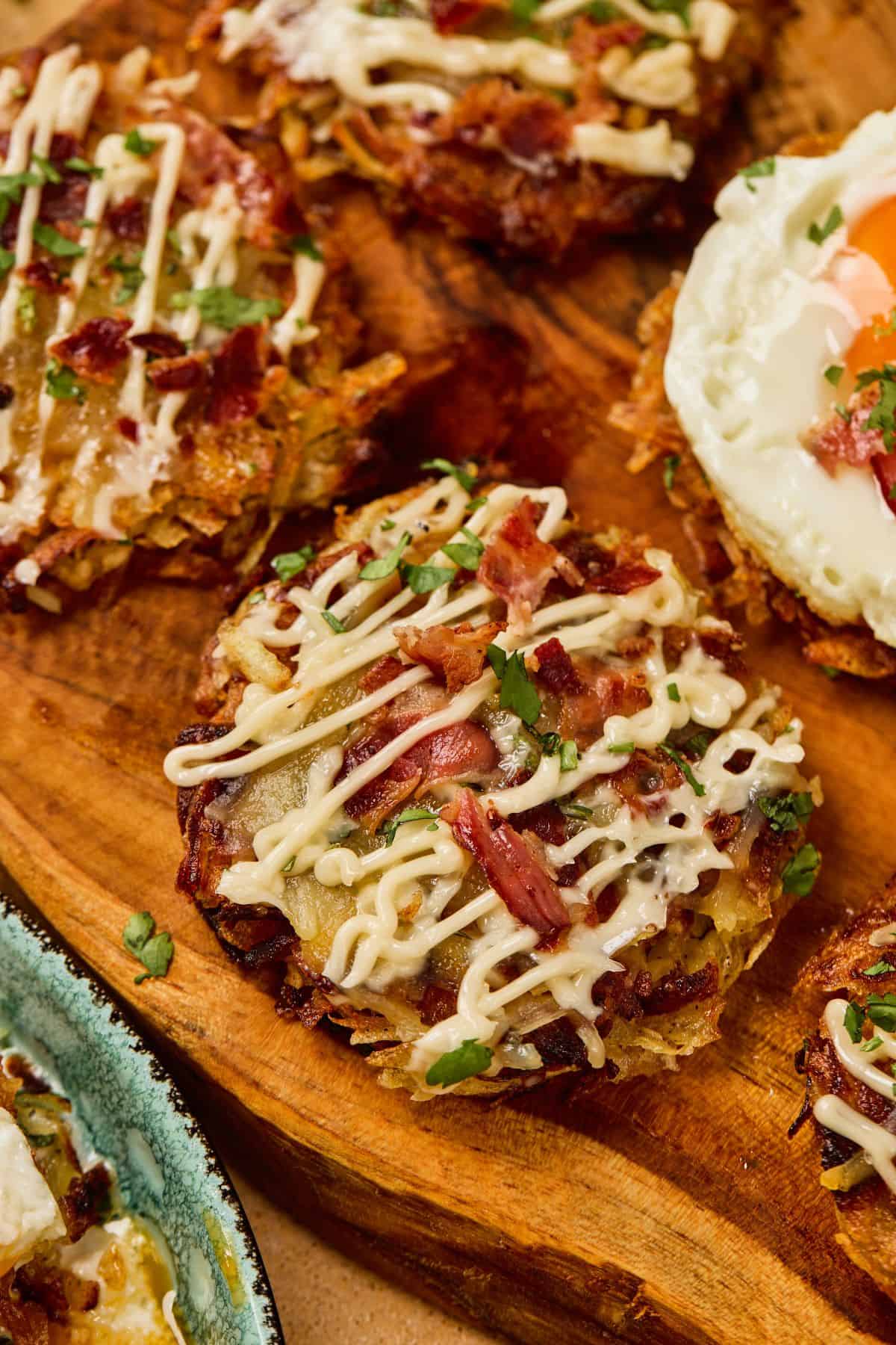 Close-up of fully loaded hashbrowns topped with melted cheddar, crispy bacon, fried eggs, green onions, and a drizzle of sour cream, surrounded by sunny side up eggs.