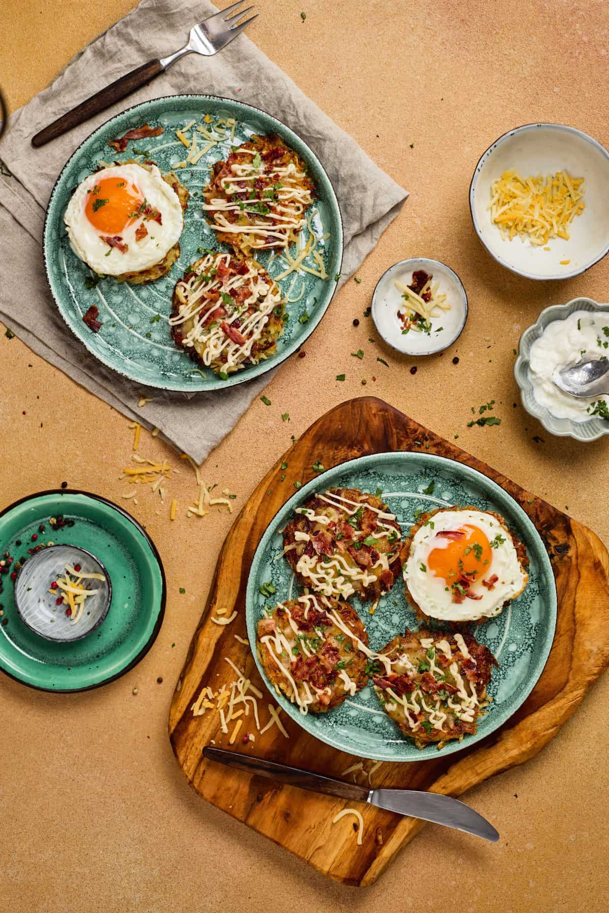 Two plates of fully loaded hashbrowns with melted cheddar, crispy bacon, green onions, sour cream, each served with a sunny side up egg.