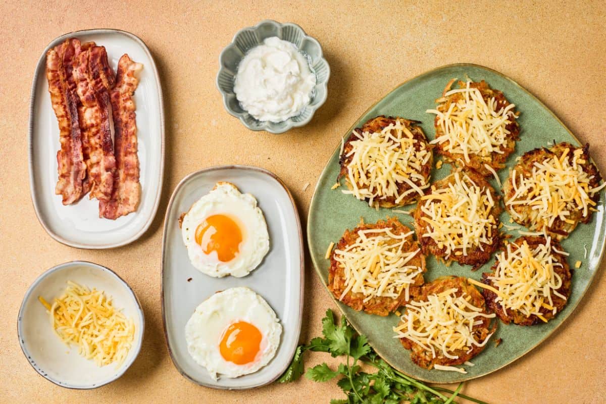 Fully loaded potato hashbrowns on a plate beside the ingredients, topped with cheese, and served with sunny side up eggs on a different plate.