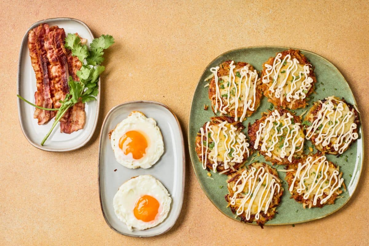 Fully loaded potato hashbrowns on a plate beside the ingredients, garnished and served with sunny side up eggs on a different plate.