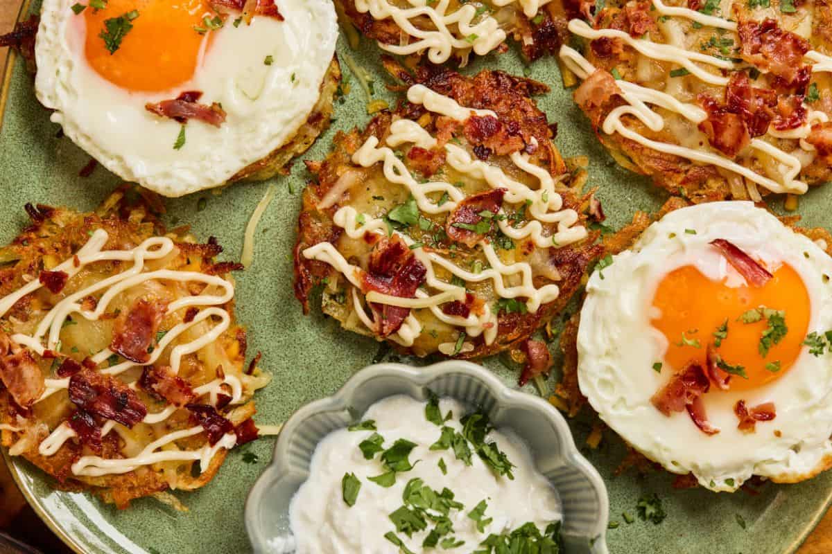 Fully loaded hashbrowns with melted cheddar, crispy bacon, green onions, and sour cream, served with a sunny side up egg on a plate.