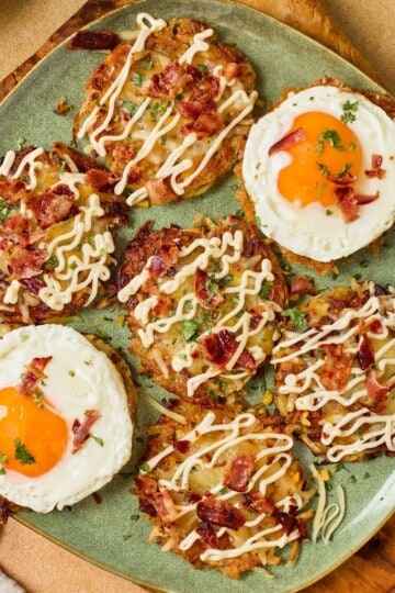 A sunny side up egg surrounded by fully loaded hashbrowns with melted cheddar, crispy bacon, green onions, and a drizzle of sour cream on a plate.