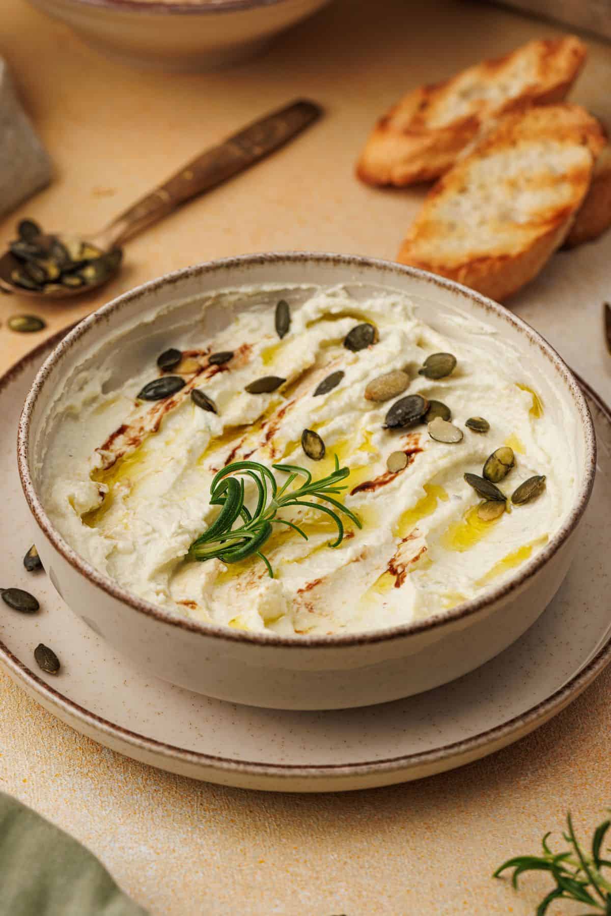 Creamy baked goat cheese dip in a bowl, garnished with crunchy nuts and herbs.