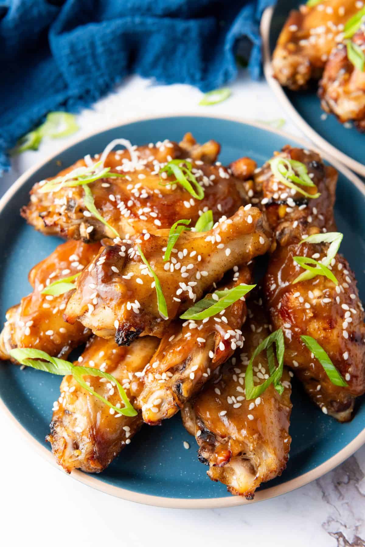 Asian baked sticky chicken wings served on a plate, garnished with sesame seeds and chopped green onions.