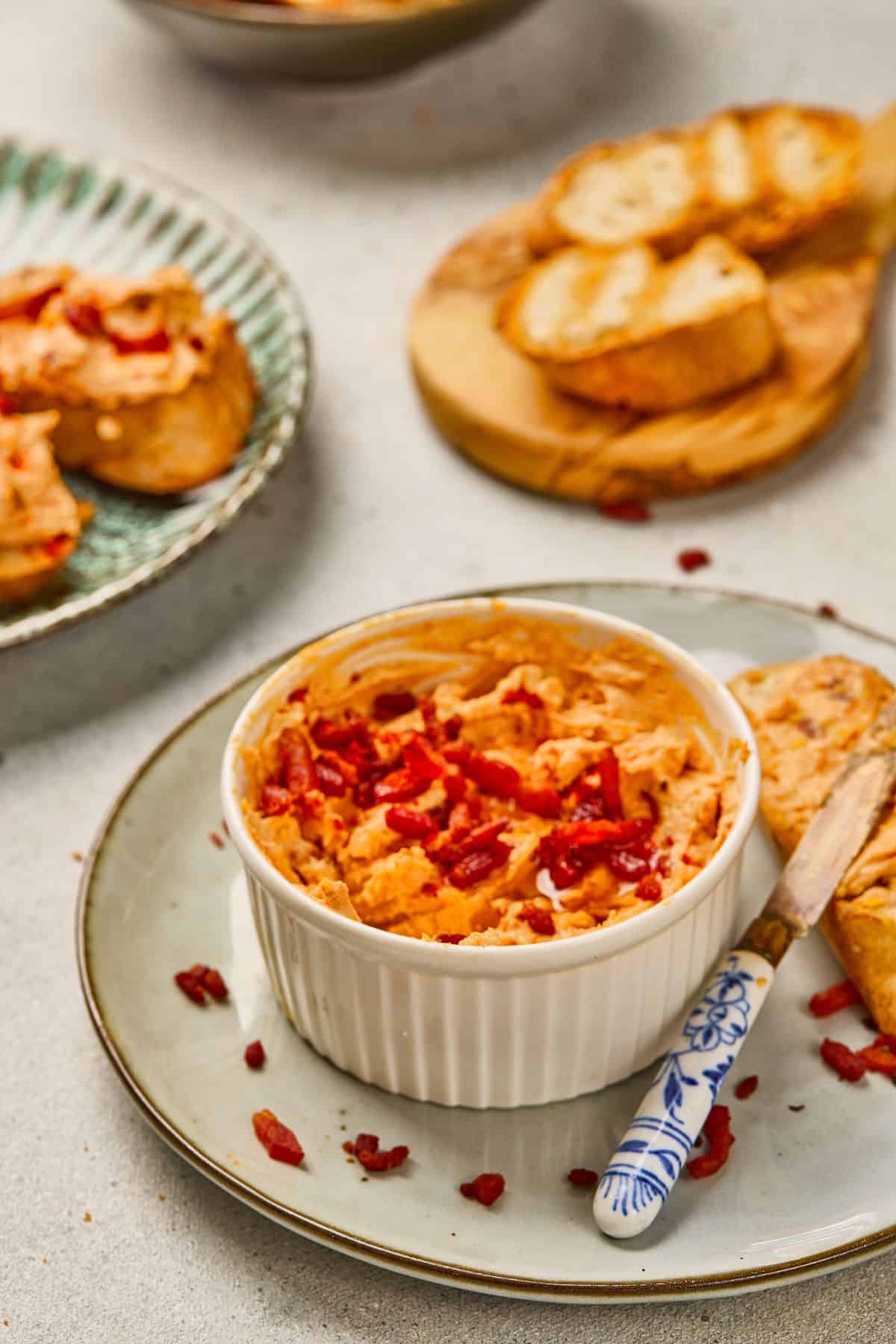 Close-up of a bowl of maple bacon cheese dip next to garlic bread with a knife on a plate.