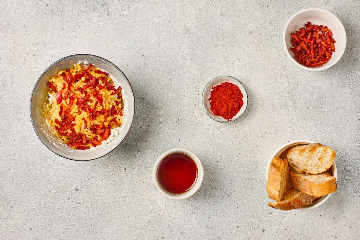 Ingredients arranged on a surface with maple bacon cheese dip being mixed in a medium bowl.