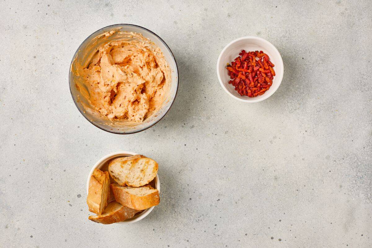 Ingredients arranged on a surface with maple bacon cheese dip being mixed in a medium bowl.