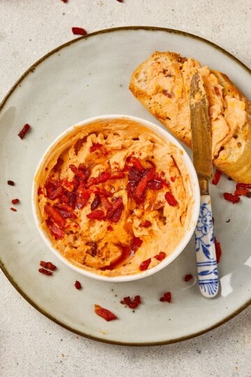 A small bowl of maple bacon cheese dip placed on a plate next to garlic bread, with a knife spreading the dip.