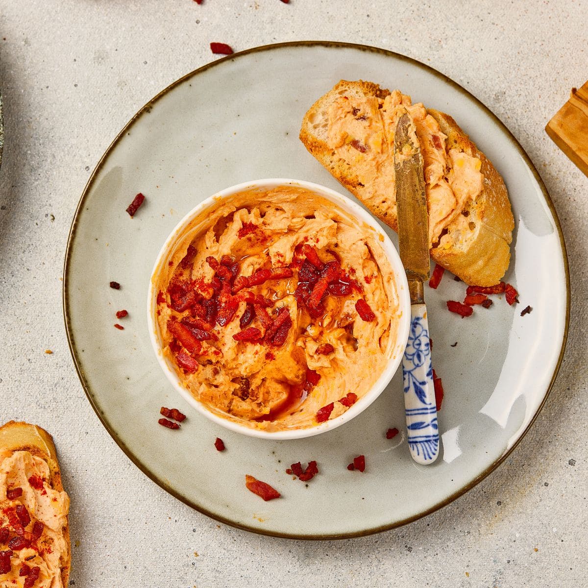 A small bowl of maple bacon cheese dip placed on a plate next to garlic bread, with a knife spreading the dip.