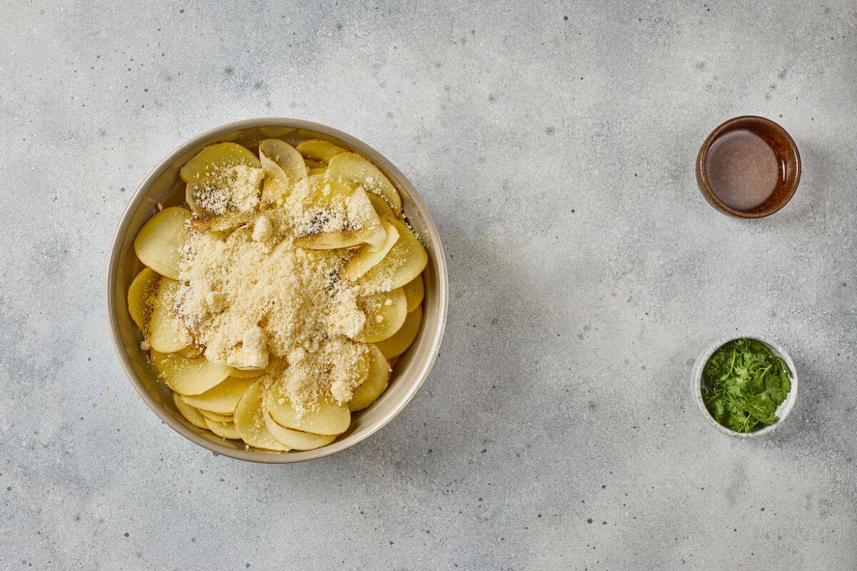 Thinly sliced potatoes in a large bowl with other ingredients on the side, ready to be seasoned.