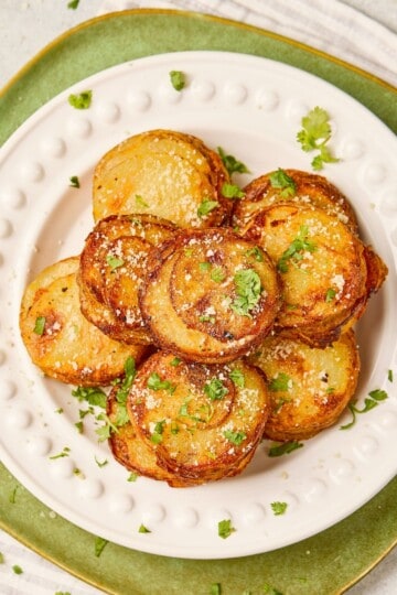 Stack of parmesan garlic potato stacks on a plate, golden brown and garnished with herbs.