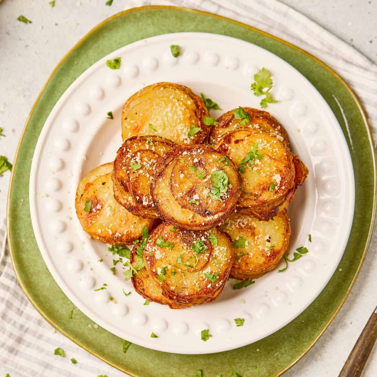 Stack of parmesan garlic potato stacks on a plate, golden brown and garnished with herbs.