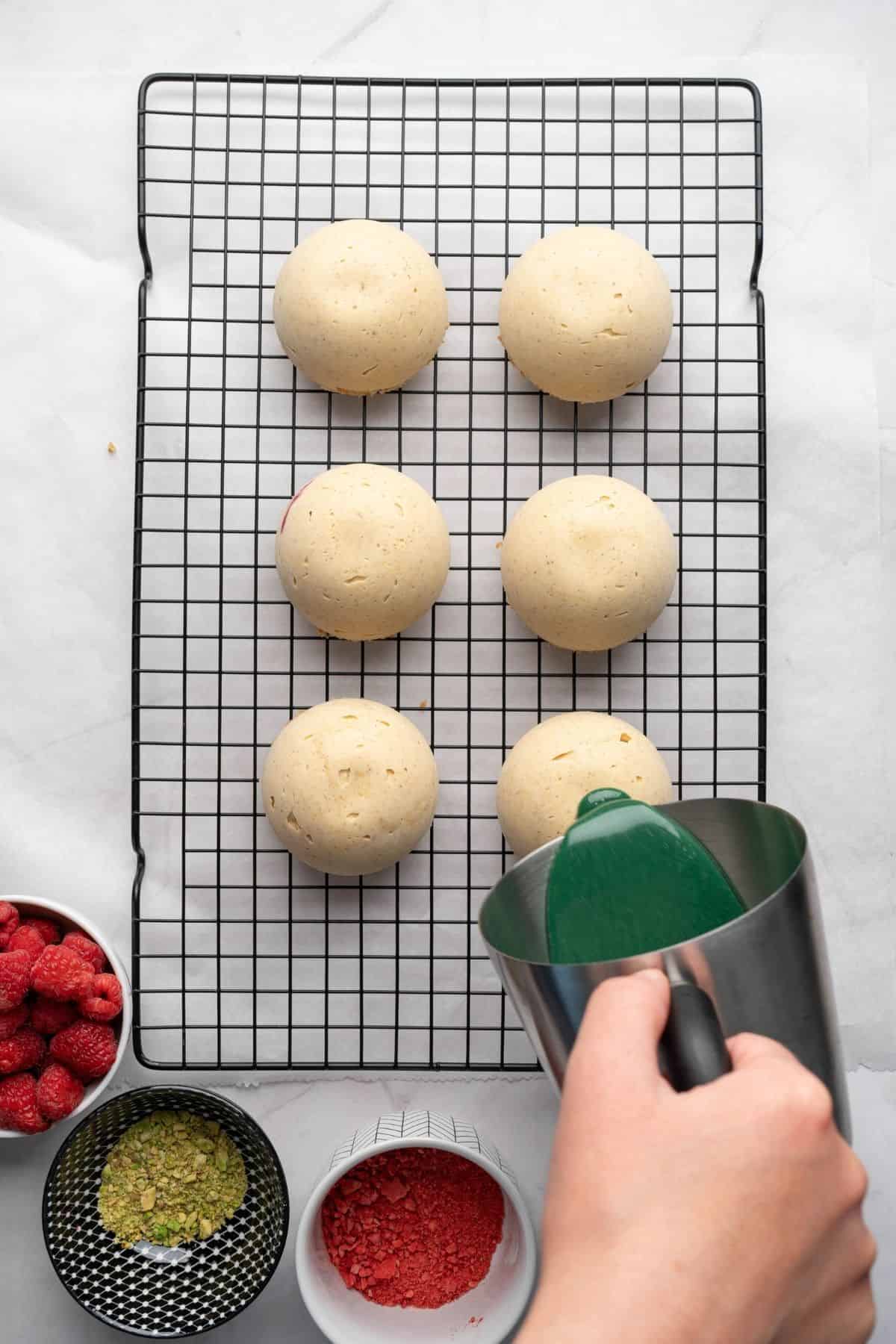 A hand pouring a green glaze over a dome-shaped dessert.