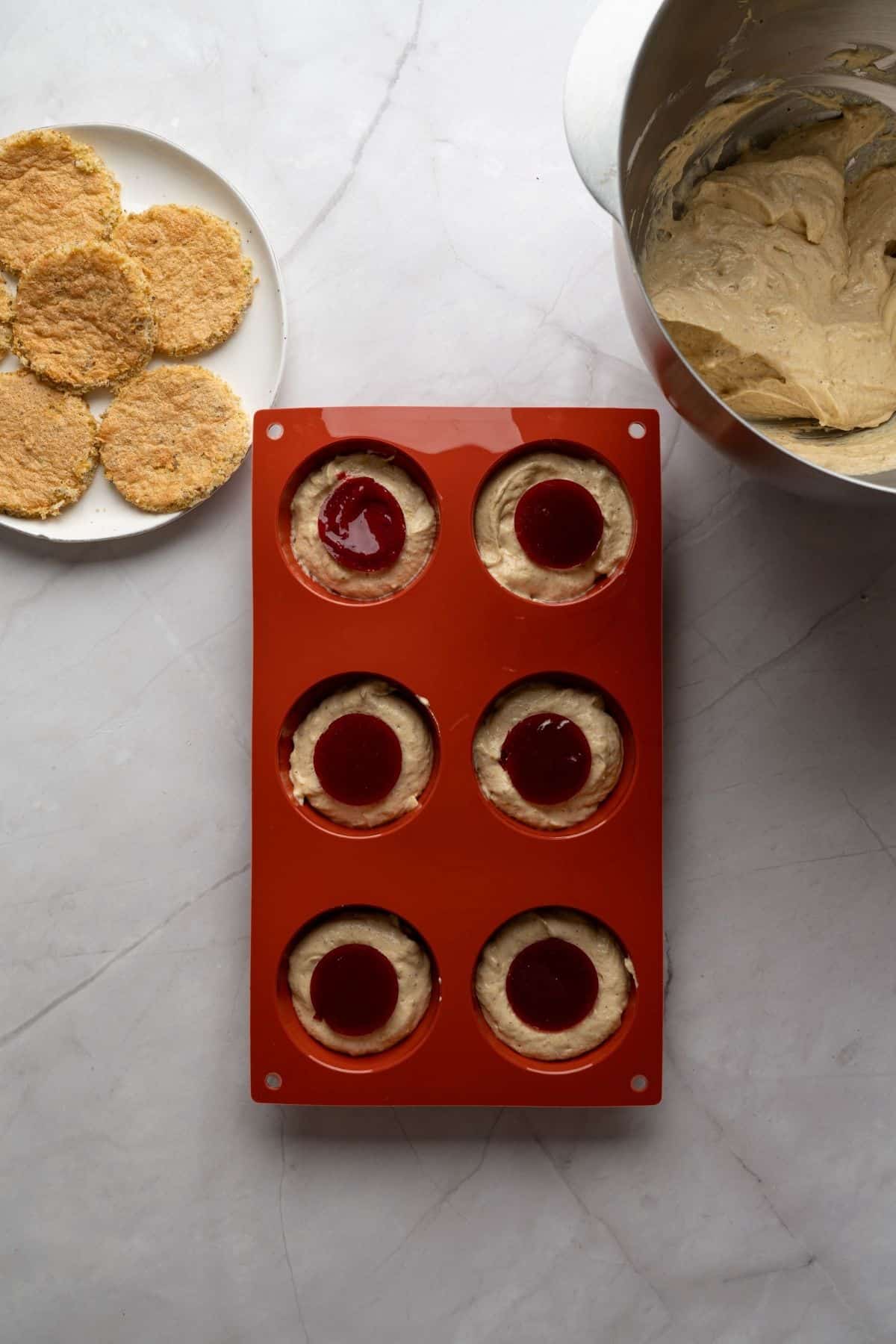 A cheesecake dome topped with red raspberry glaze, placed in a baking pan.