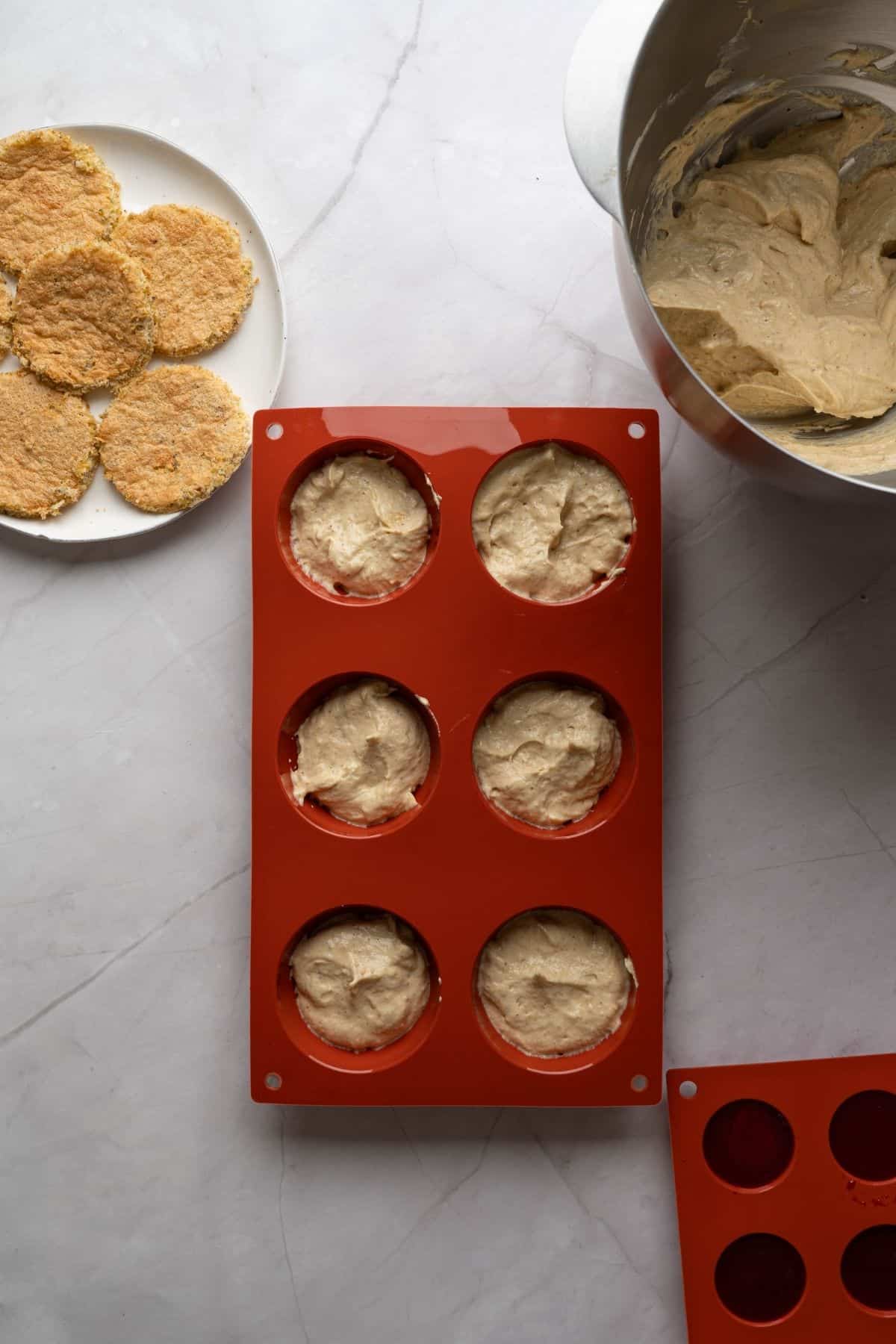 A pistachio cheesecake mixture placed in a baking pan, surrounded with bowls of raspberries, pistachios, and other ingredients.