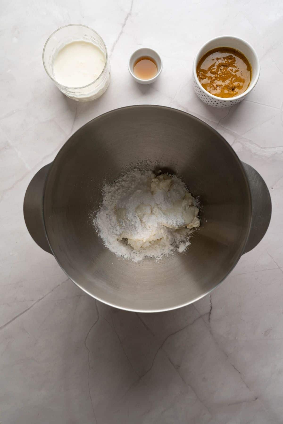 Ingredients being mixed in a large mixing bowl with other ingredients placed beside it.
