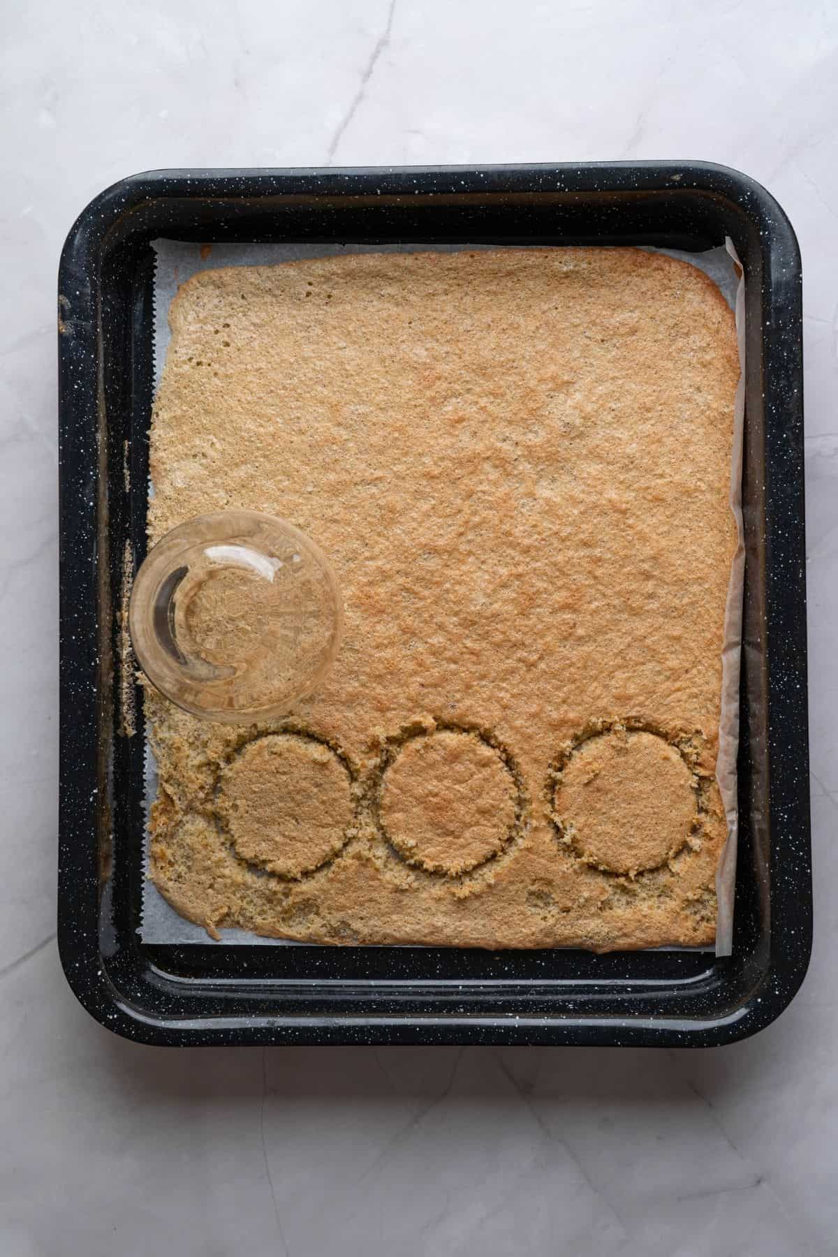 A flattened pistachio sponge layer being shaped on a baking sheet, ready for baking.