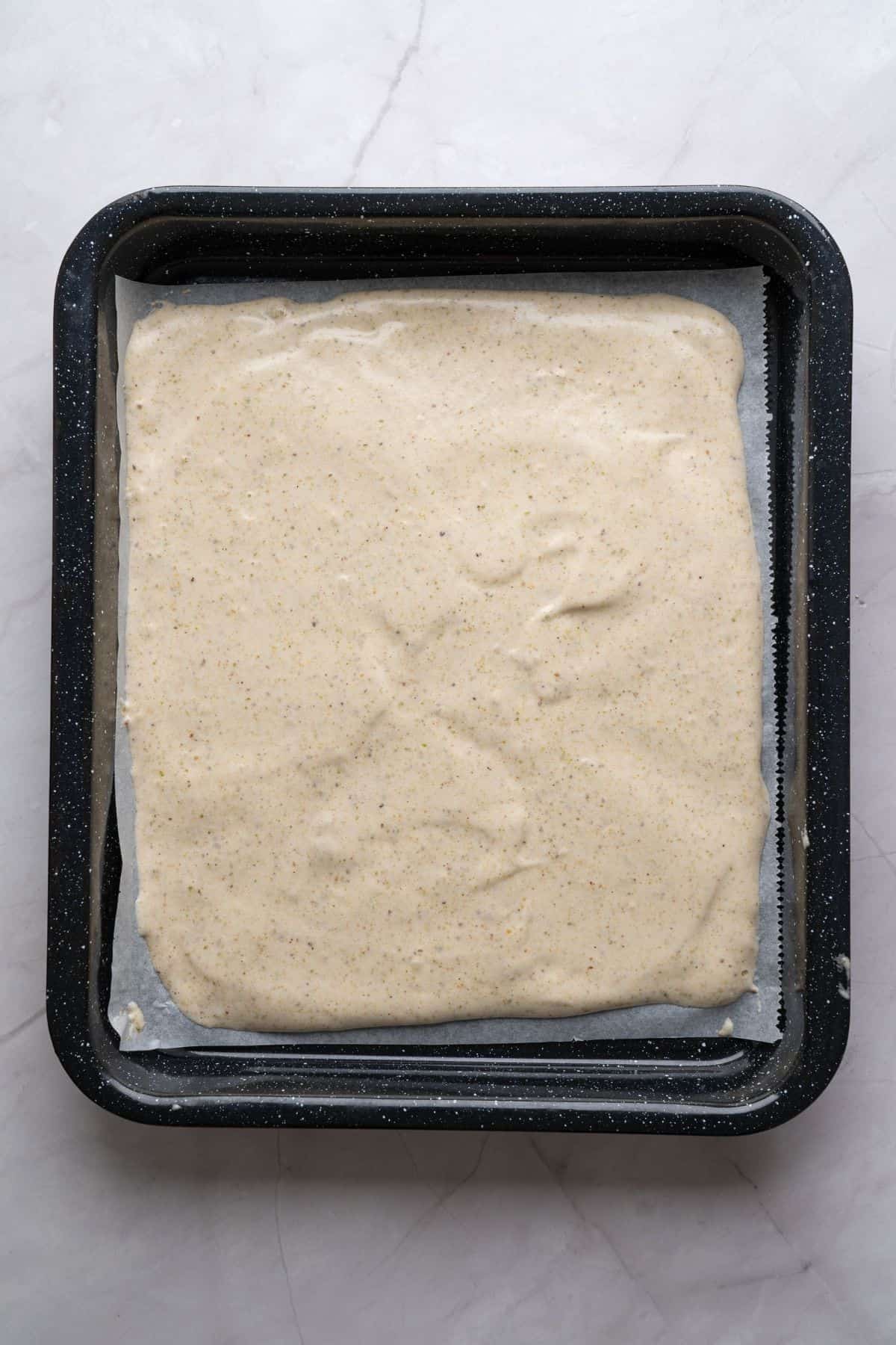 An unbaked, flattened pistachio sponge layer on a baking sheet.